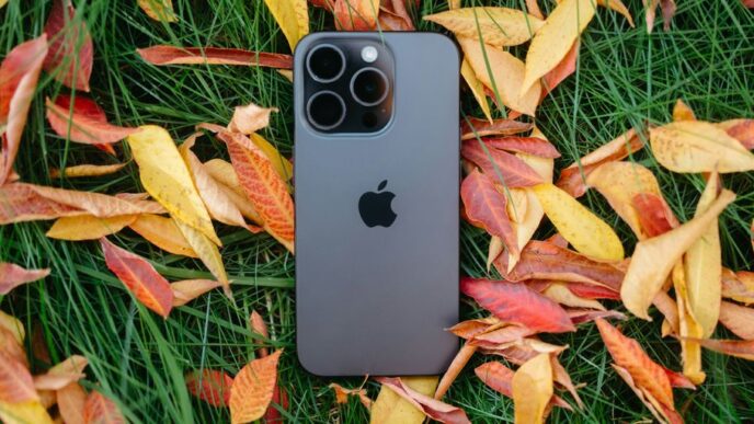 An iPhone is laying in the grass surrounded by autumn leaves
