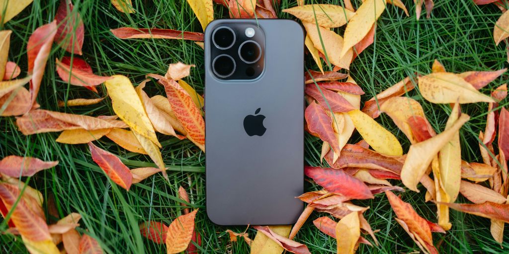 An iPhone is laying in the grass surrounded by autumn leaves