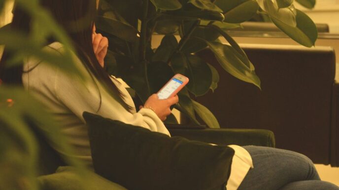 person using smartphone while sitting on black sofa between green plants