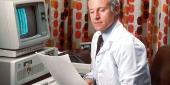 man reading papers in front of computer