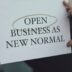 a person holding a sign that says open business as new normal