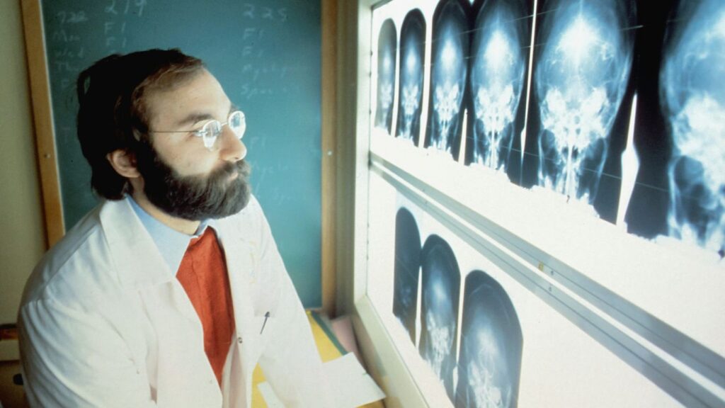 a man in a lab coat and tie looking at an x - ray