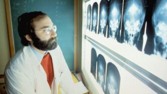 a man in a lab coat and tie looking at an x - ray