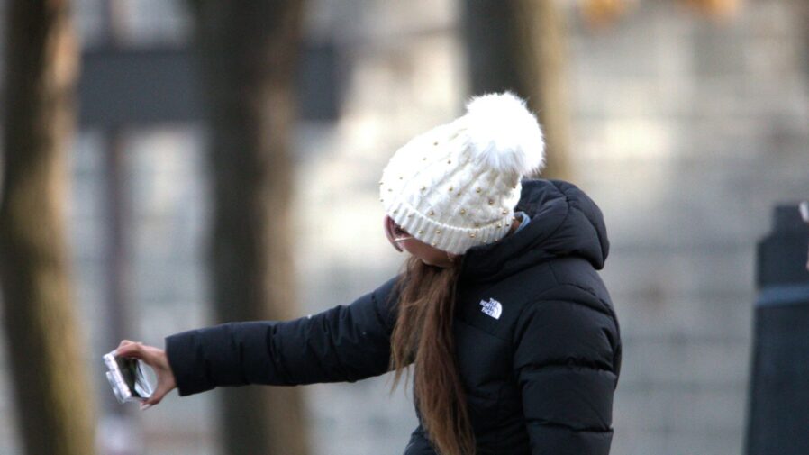a woman in a black jacket and a white hat holding a cell phone