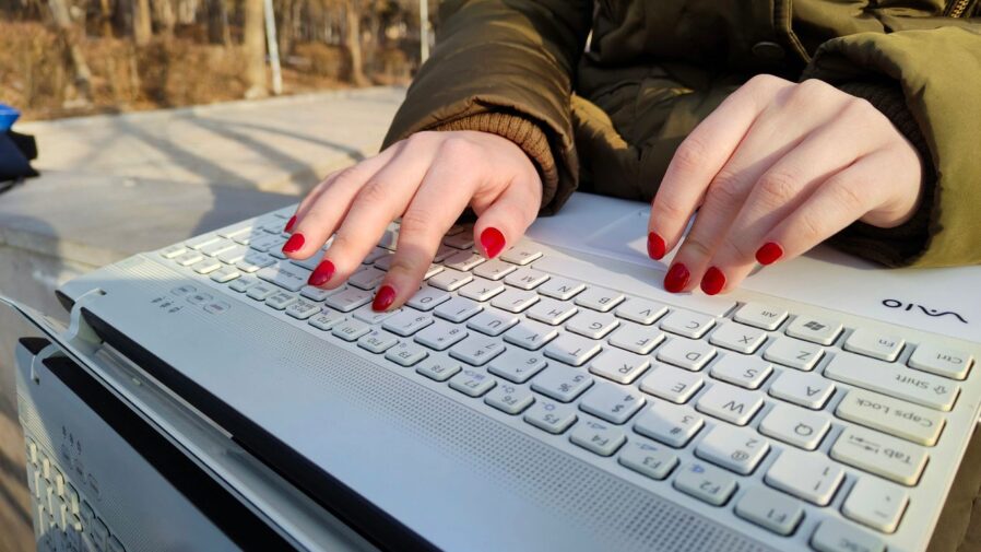 a woman with red nails typing on a white keyboard