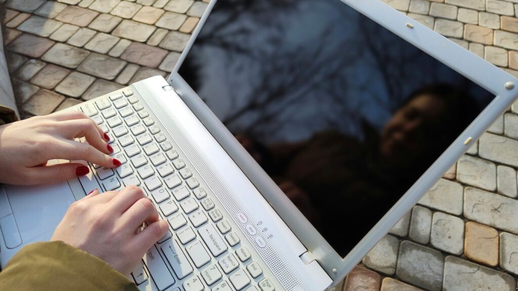 a woman is typing on a laptop outside