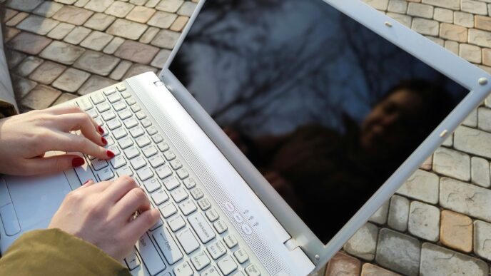 a woman is typing on a laptop outside