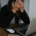 a woman covering her face while looking at a laptop
