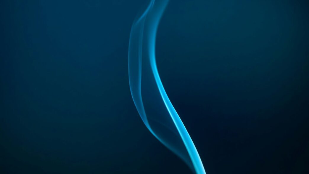 Blue smoke gracefully rising against the dark.