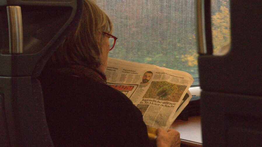 A woman reads a newspaper on a train.