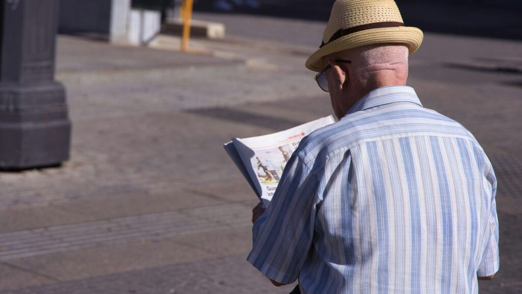 a man in a hat is reading a newspaper