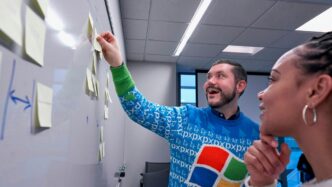 man wearing blue Windows sweater holding sticky note on white board