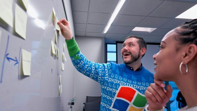 man wearing blue Windows sweater holding sticky note on white board