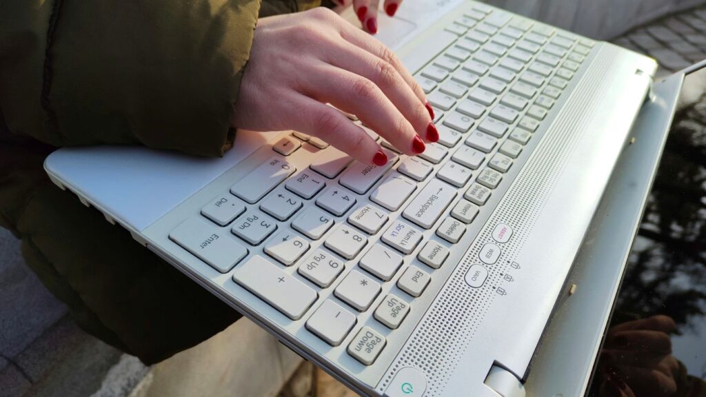 a woman is typing on a laptop outside
