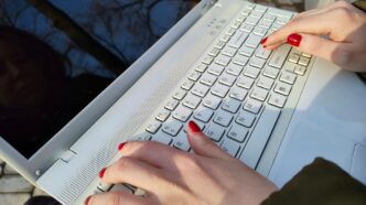 a woman is typing on a laptop outside