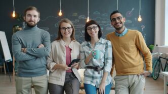 Four smiling people standing in a modern office.