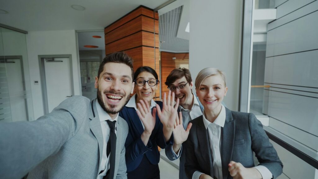 Four business people smiling and waving at camera.