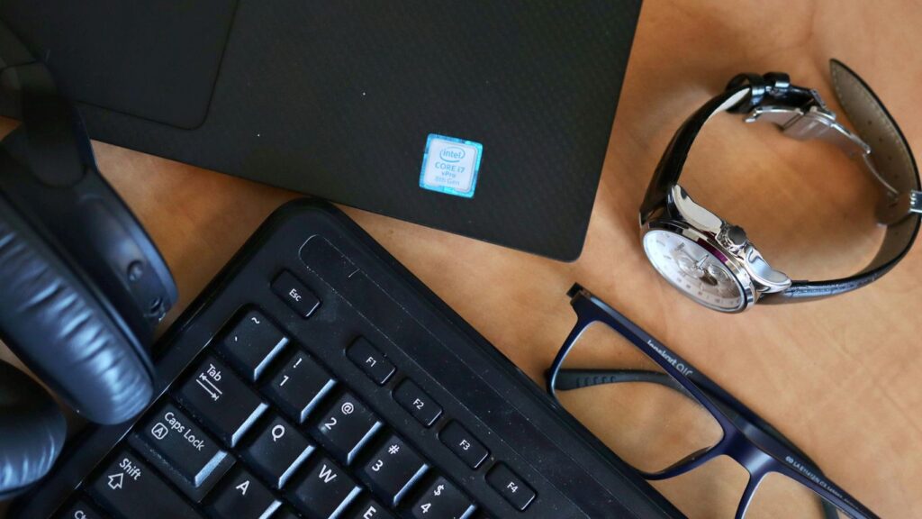 a desk with a keyboard, glasses and a laptop