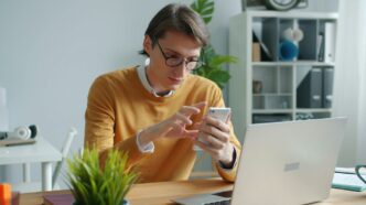 Man in yellow sweater using smartphone at desk