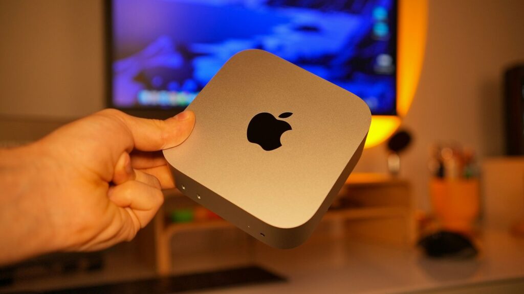 Hand holding a small silver apple computer.