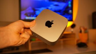 Hand holding a small silver apple computer.