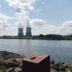 a body of water with a group of smokestacks in the distance