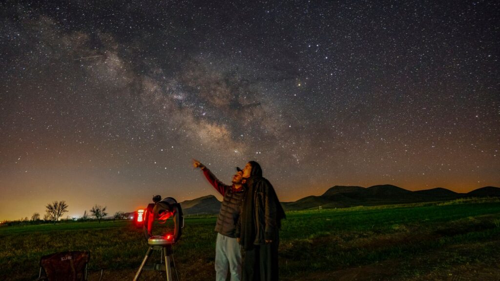 a man standing next to a telescope looking at the stars