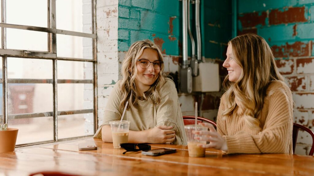 two women sitting at a wooden table talking