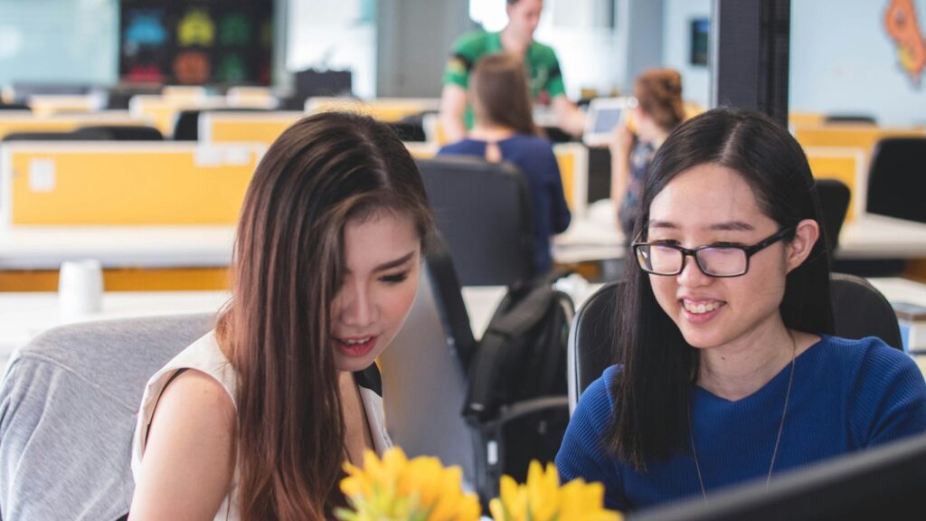 two women smiling in front of computer monitor