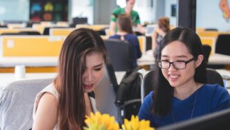 two women smiling in front of computer monitor