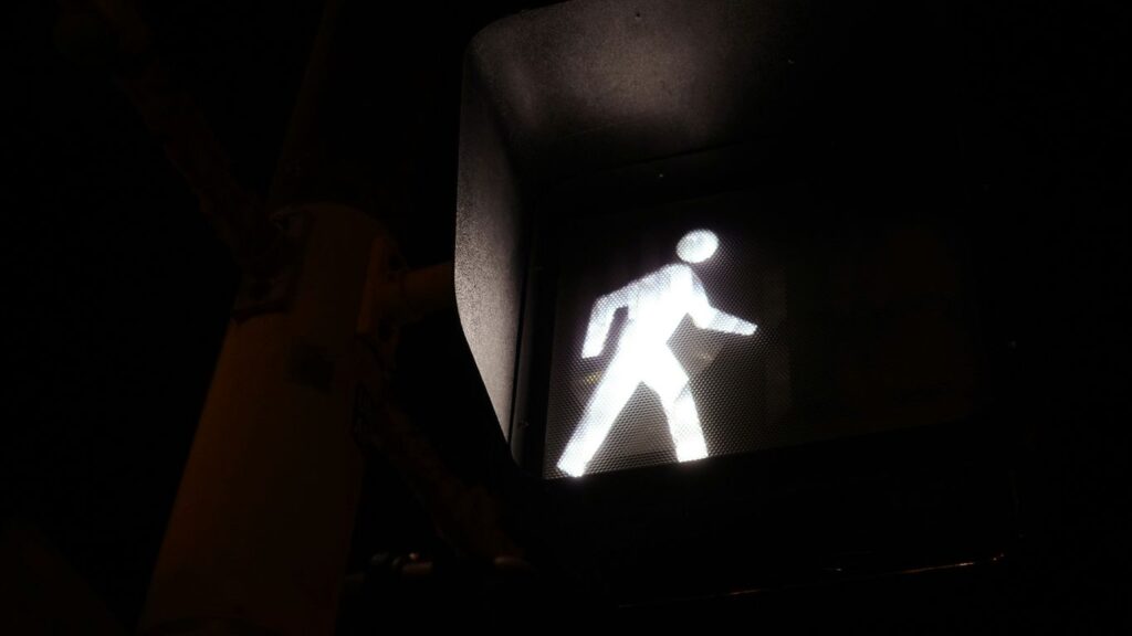 a traffic light with a white pedestrian sign on it