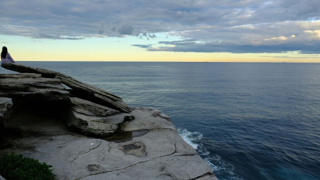 A person standing on top of a cliff next to the ocean