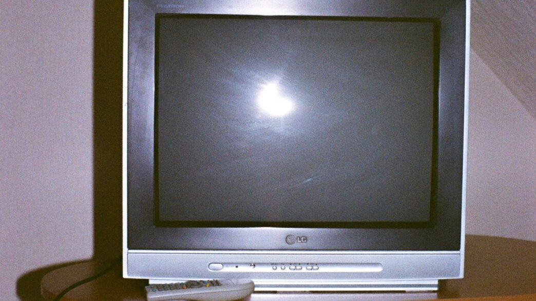 A television set with a remote control on a table.