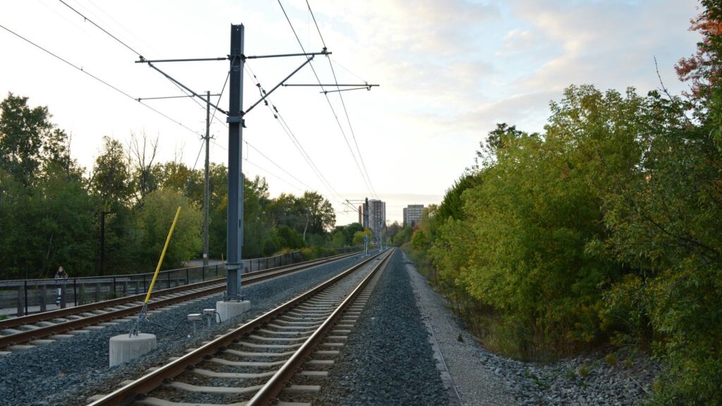 Train tracks leading towards distant buildings through trees.