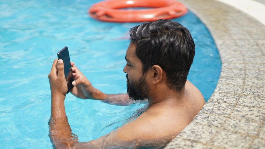 man in swimming pool holding smartphone