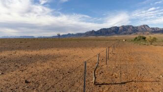 a fence in the middle of a desert with mountains in the background