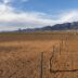 a fence in the middle of a desert with mountains in the background