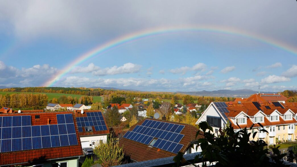 Rainbow over a suburban neighborhood with solar panels.