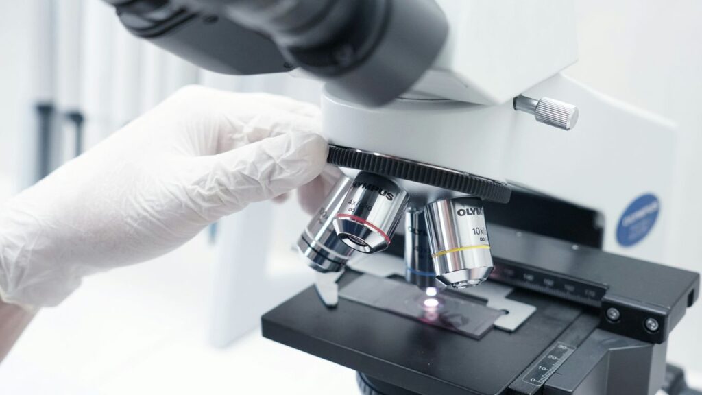 A person in white gloves looking through a microscope