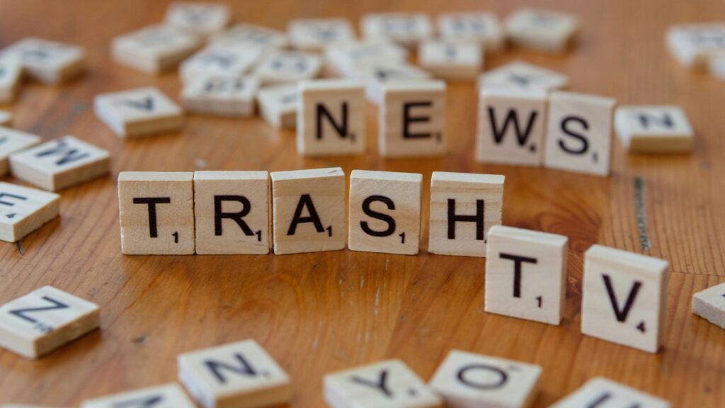 A wooden table topped with scrabble tiles spelling news, trash, TV and