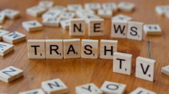 A wooden table topped with scrabble tiles spelling news, trash, TV and