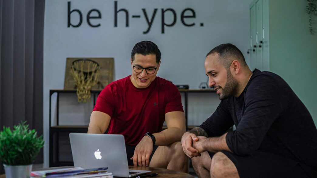 Two men sitting on a coffee table looking at a laptop