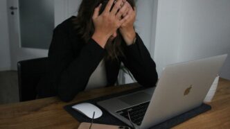 a woman covering her face while looking at a laptop