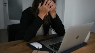 a woman covering her face while looking at a laptop