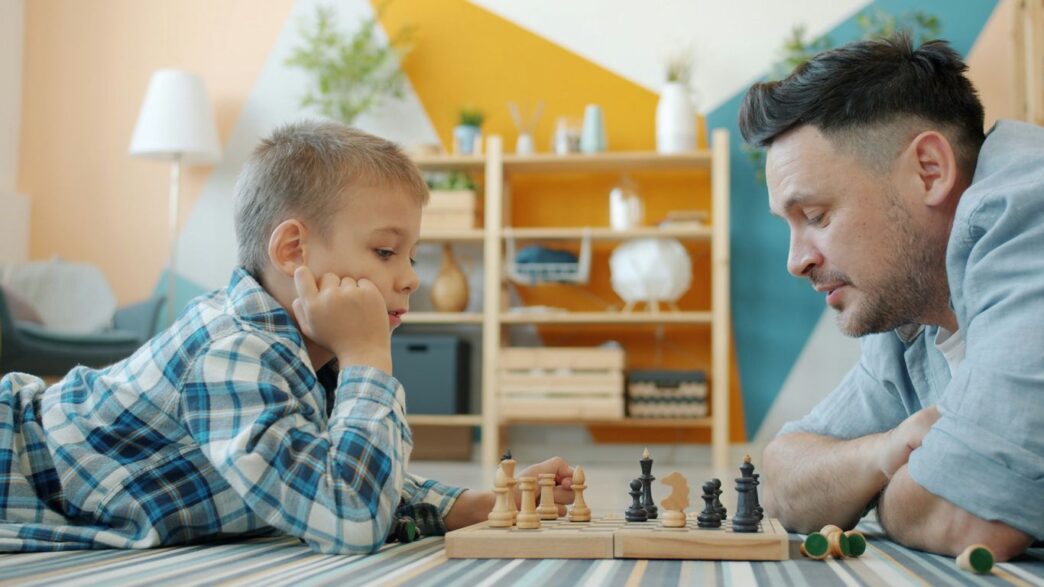 Father and son playing chess on the floor.