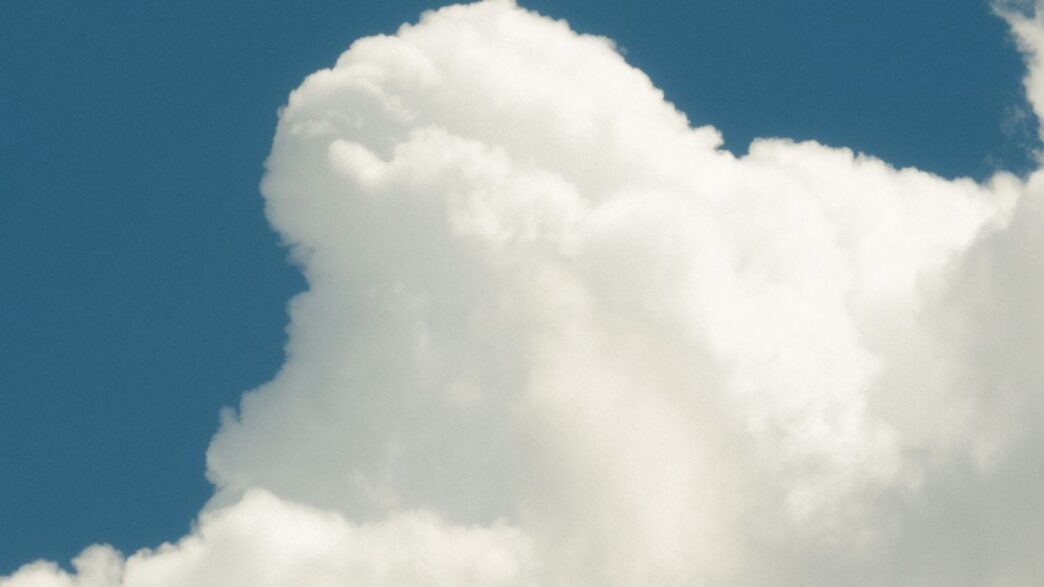 a jet flying through a cloudy blue sky