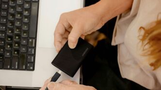 A person holding a cell phone in front of a laptop