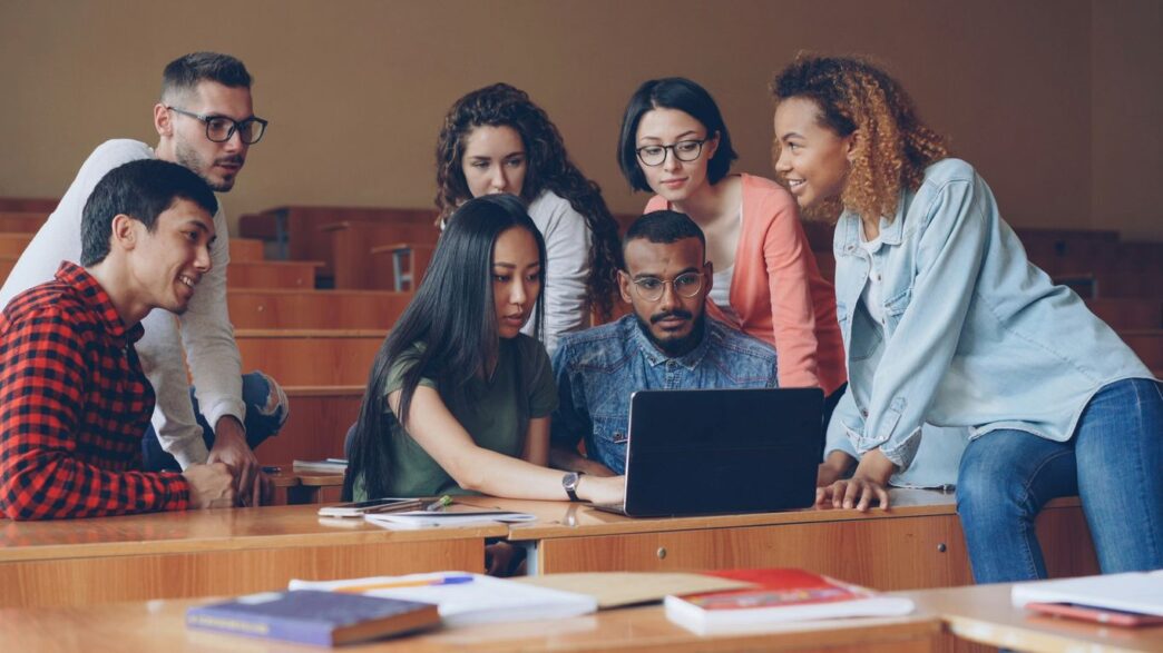 Diverse group of students gathered around a laptop.