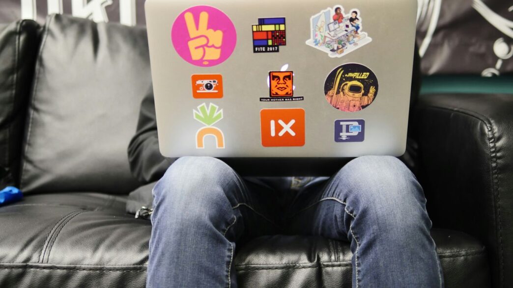 man using silver MacBook sitting on black leather sofa