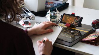 person holding sketch pad while watching on smartphone